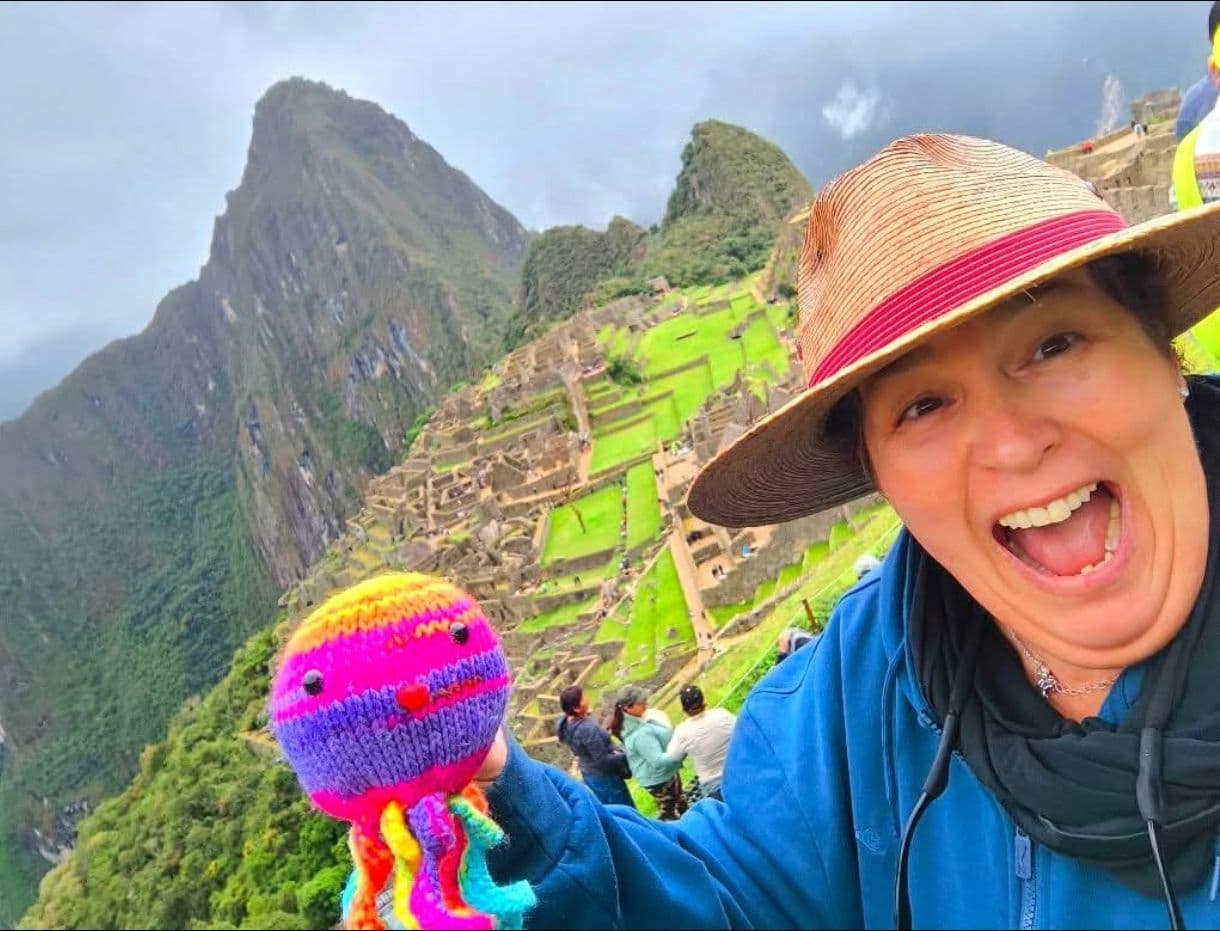 Machu Picchu ruins with a traveler holding a colorful knitted octopus, Cusco region, Peru.