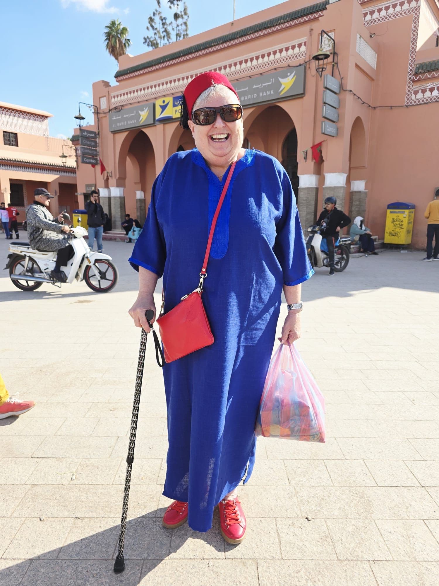Woman in a blue robe holding a cane and a shopping bag in Jemaa el-Fnaa, Marrakech, Morocco.