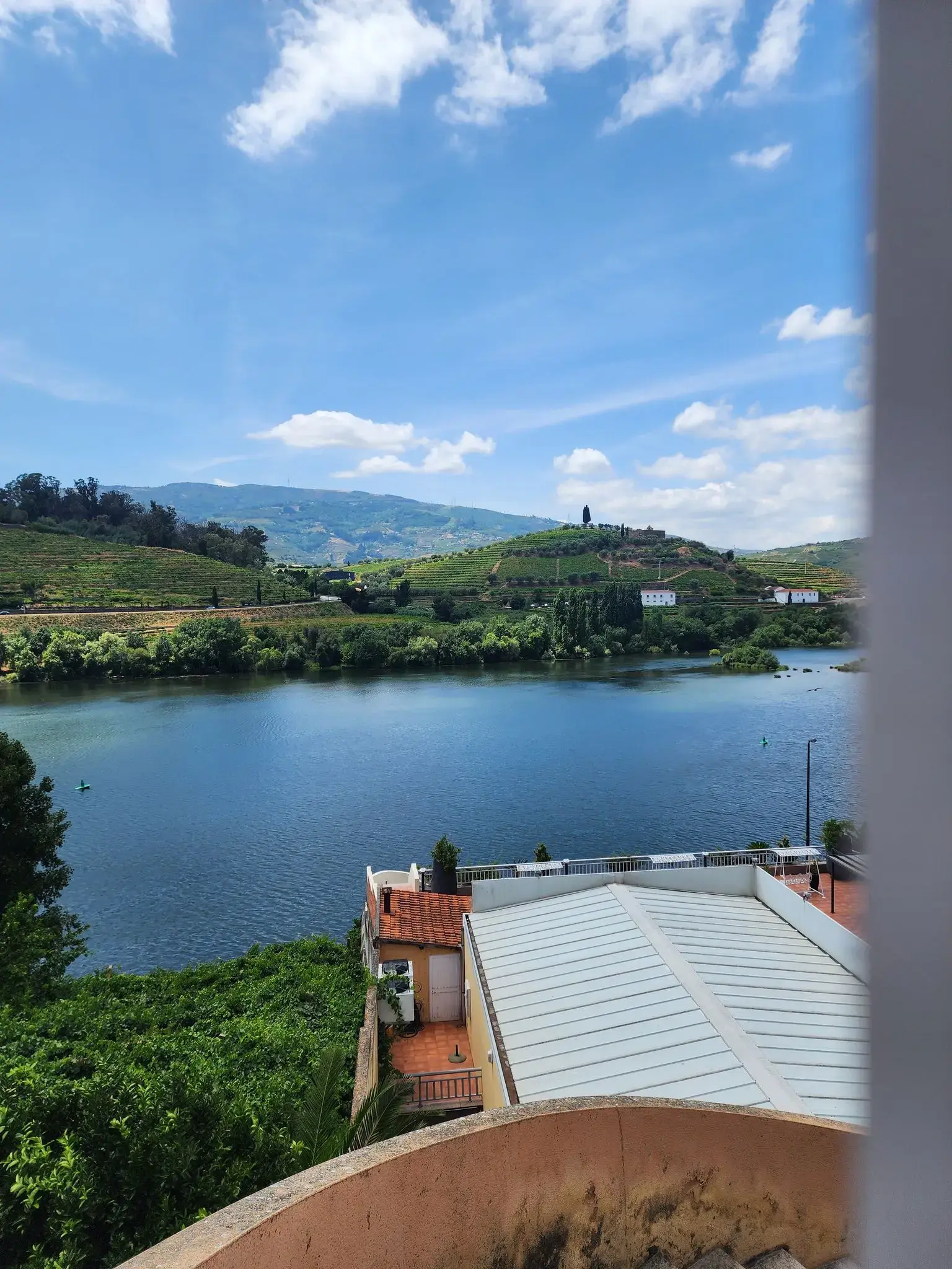 Wide view of a calm river with terraced vineyards and hillside houses under a blue sky, Portugal.