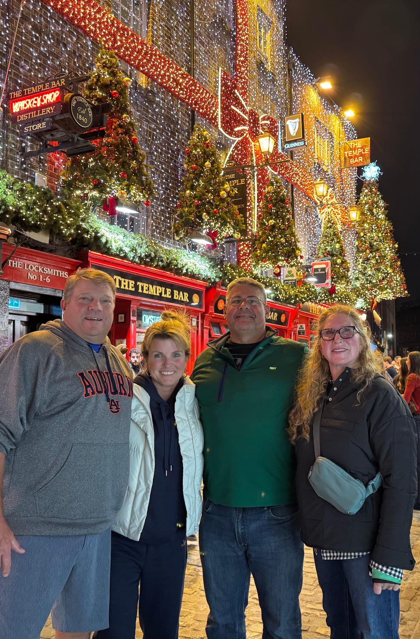 The Temple Bar facade lit with Christmas lights, four friends posing in front, Dublin, Ireland.