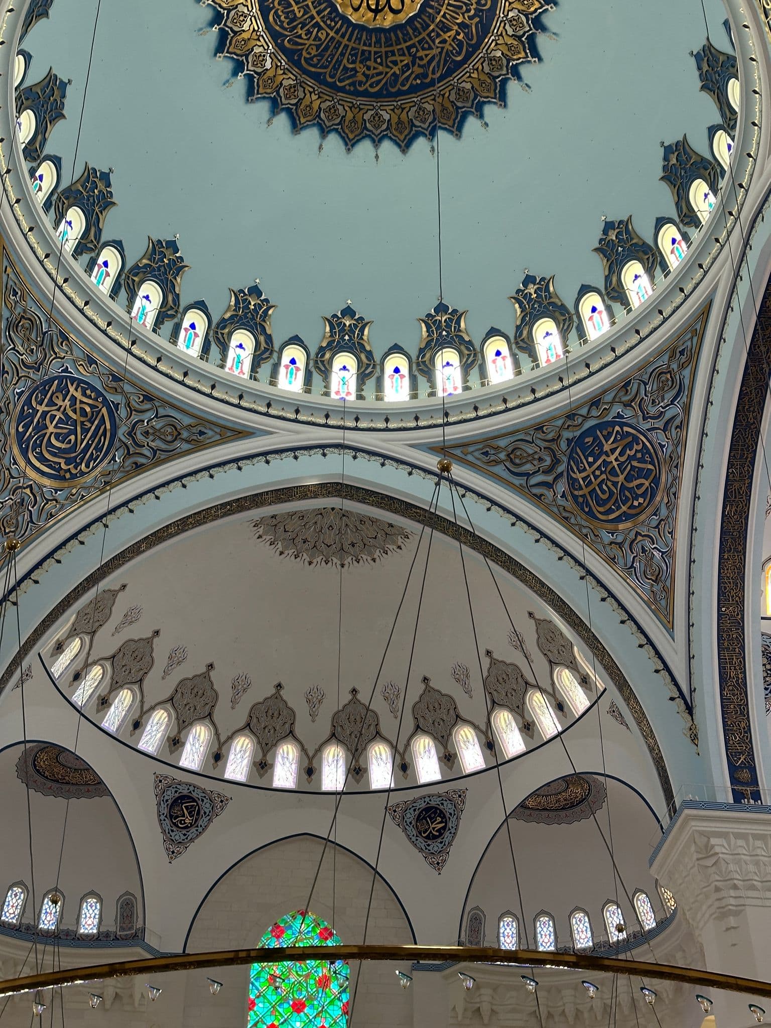 Interior dome of Çaml?ca Mosque in Istanbul, Turkey, with ornate blue and gold calligraphy and arched stained-glass windows.