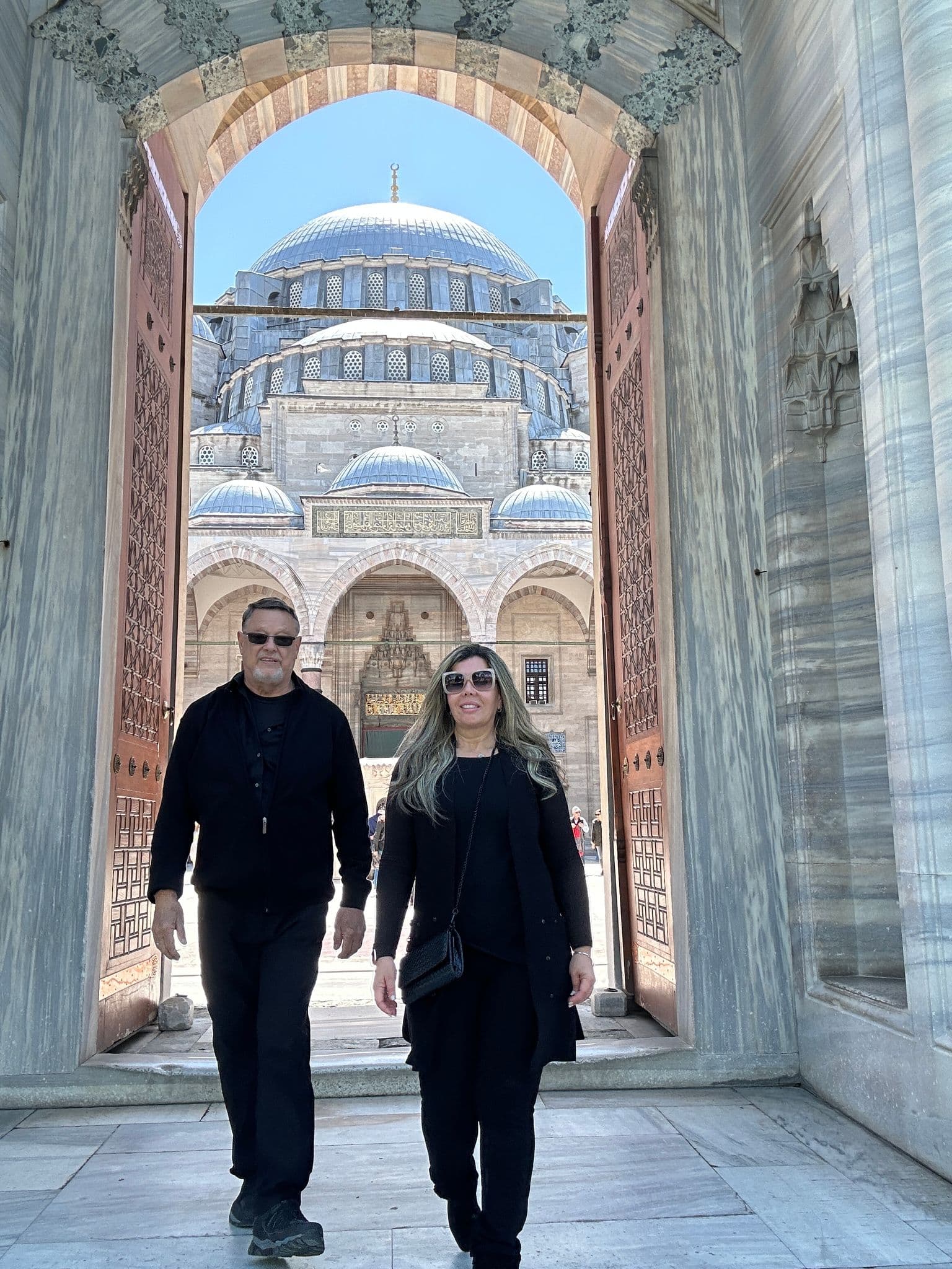 Süleymaniye Mosque framed by its arched entrance with two travelers walking through the doorway in Istanbul, Turkey.