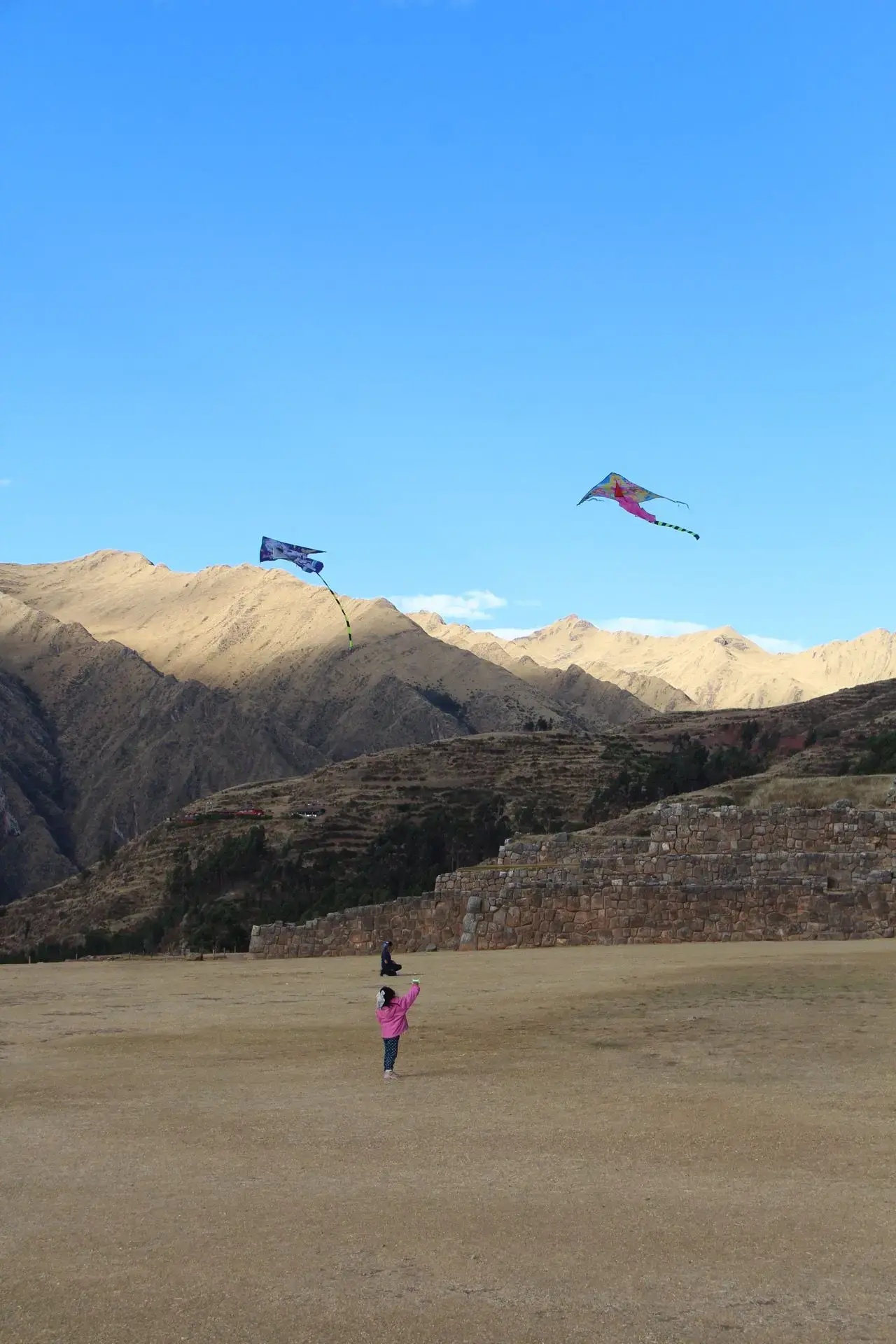 Chinchero archaeological terraces with colorful kites flying overhead and a child holding a kite on the field, Sacred Valley, Peru.