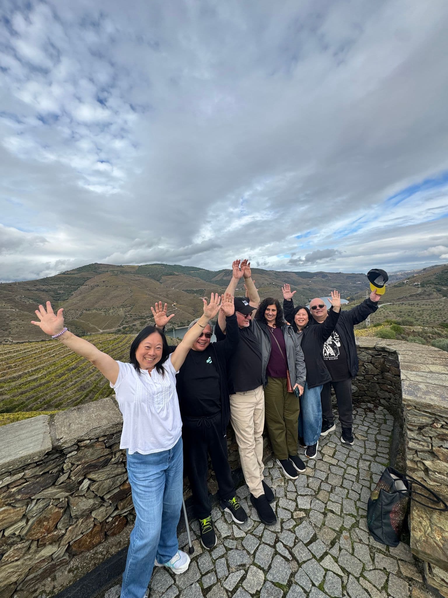 Terraced vineyards in the Douro Valley with a group of friends raising their hands on a stone viewpoint, Portugal.
