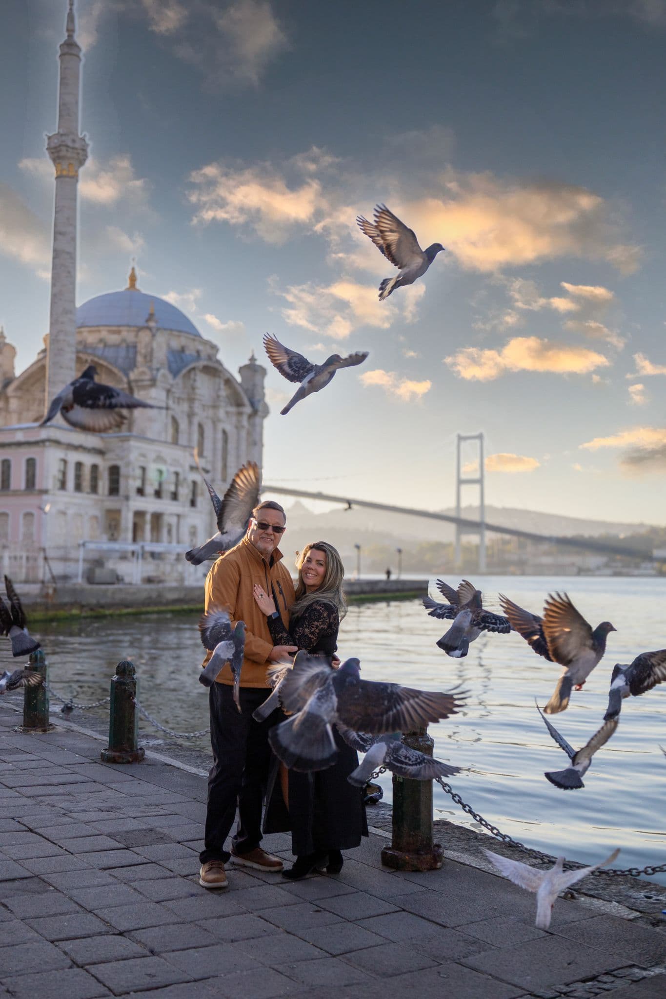 Ortaköy Mosque near the Bosphorus with pigeons in flight as a couple stands on the waterfront in Istanbul, Turkey.