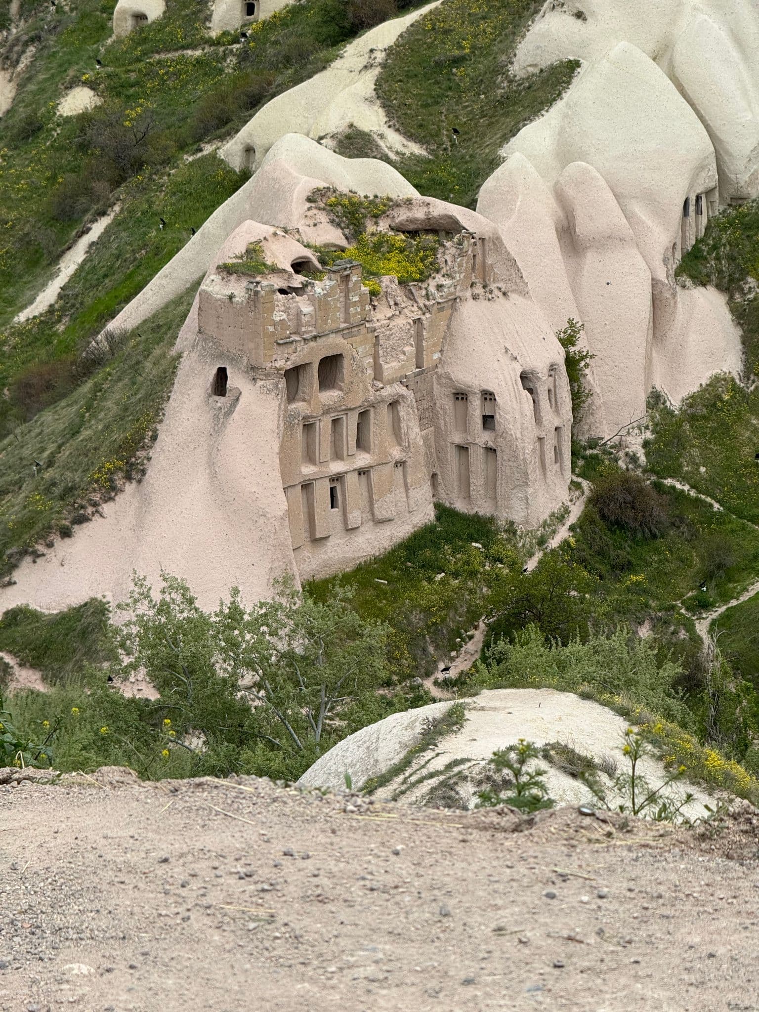 Uçhisar rock-cut dwellings carved into fairy-chimney cliffs in Cappadocia, Turkey, seen from a dirt overlook.