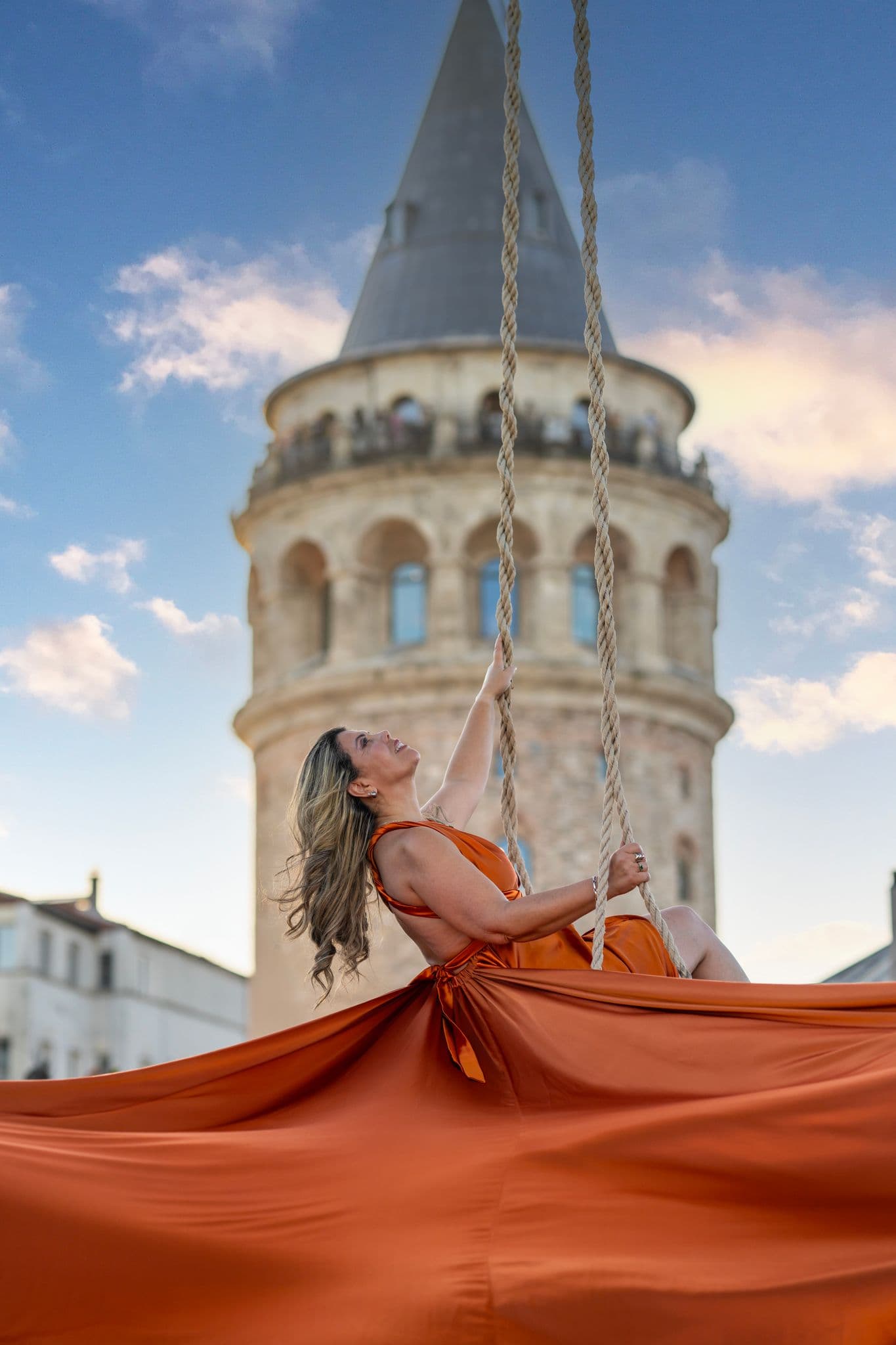 Galata Tower framed behind a woman on a rope swing wearing a flowing orange dress in Istanbul, Turkey