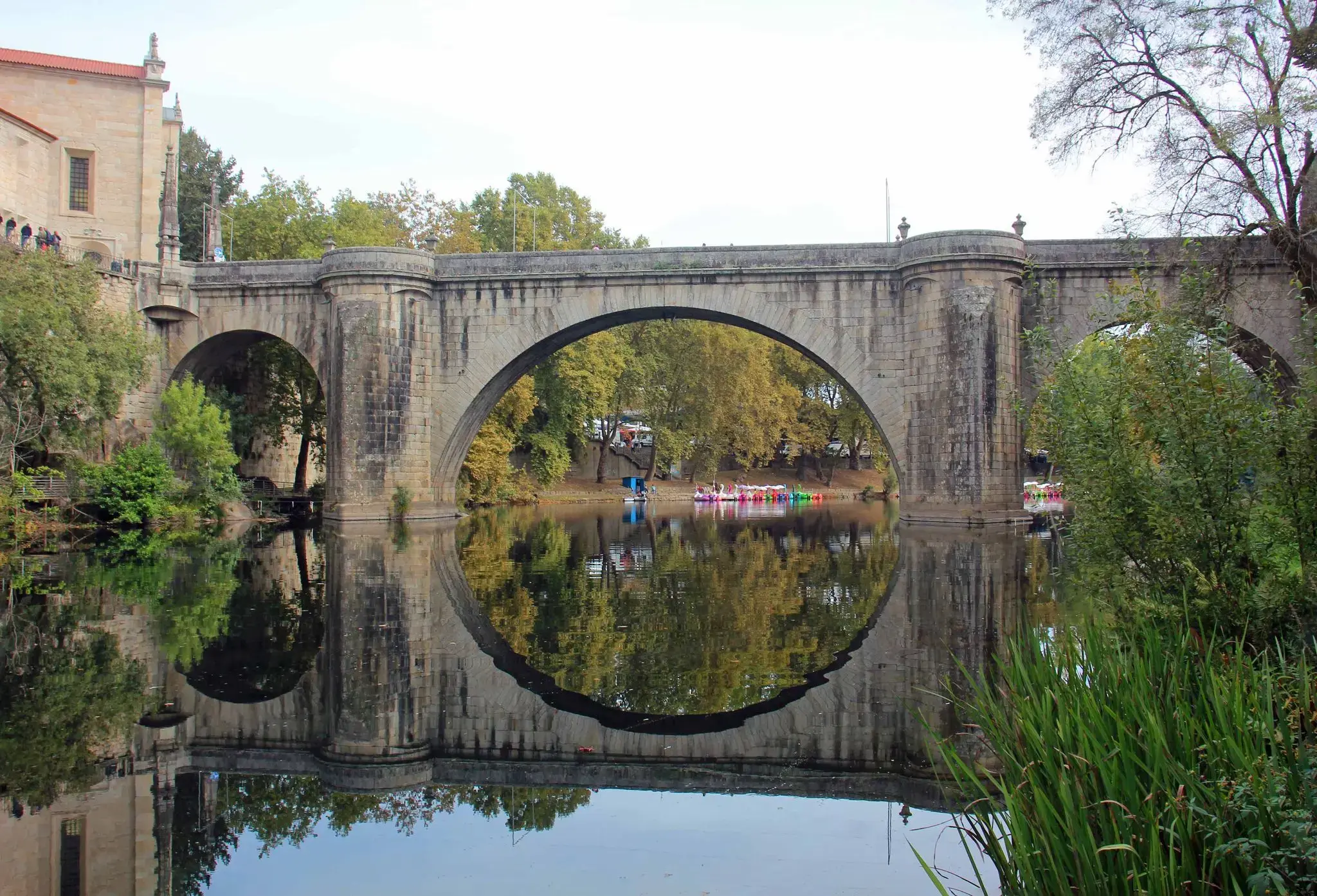 São Gonçalo Bridge in Amarante, Portugal, arching over the Tâmega River with its circular reflection and colorful paddle boats at the far bank.
