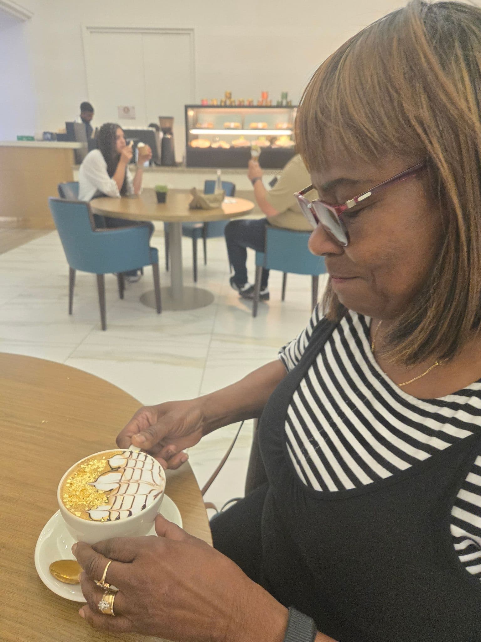Woman holding a gold-topped cappuccino at a hotel cafe table in Abu Dhabi, United Arab Emirates.