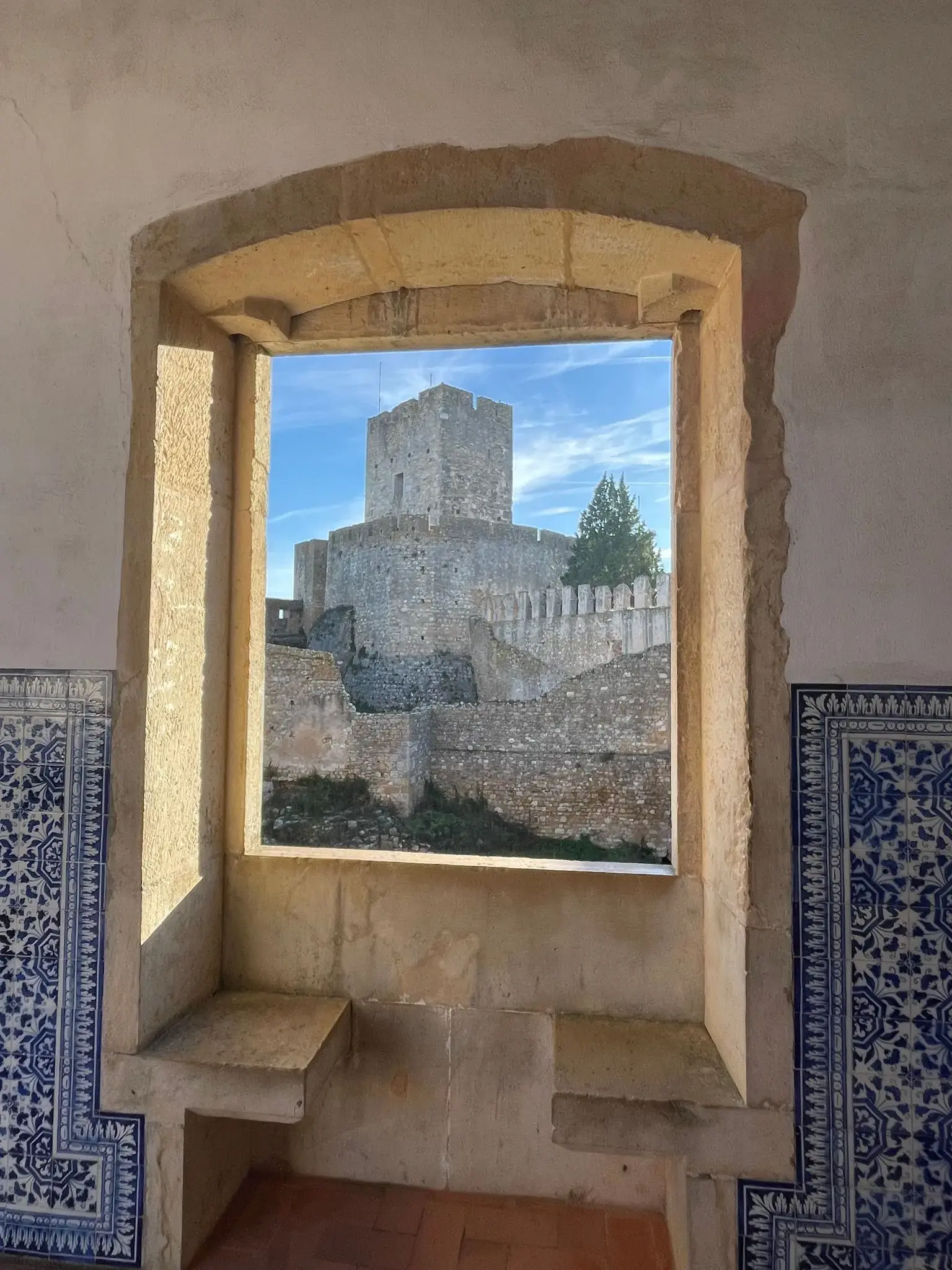 Convent of Christ tower framed by a stone window with blue azulejo tiles, Tomar, Portugal