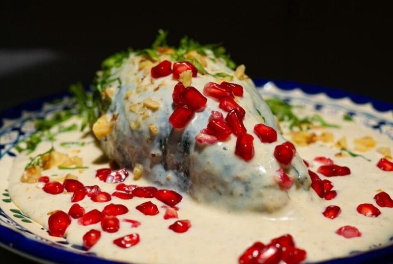 Delicious Mexican Chiles en Nogada garnished with pomegranate seeds on a decorative plate.
