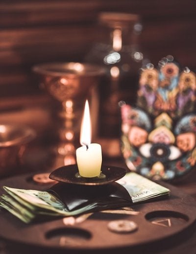 A single candle flame illuminates esoteric objects including tarot cards and crystals