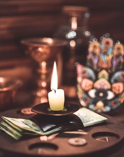 A single candle flame illuminates esoteric objects including tarot cards and crystals