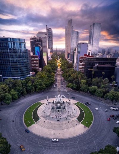 Stunning aerial perspective of Mexico City's iconic Angel of Independence monument surrounded by modern skyscrapers and tree-lined boulevards at golden hour