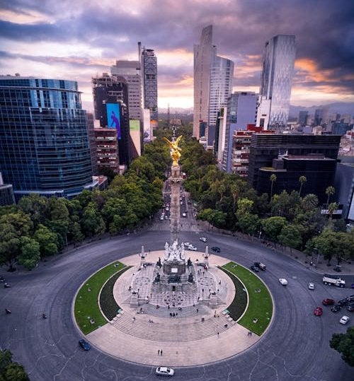 Stunning aerial perspective of Mexico City's iconic Angel of Independence monument surrounded by modern skyscrapers and tree-lined boulevards at golden hour