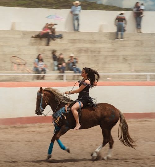 A skilled female rider in traditional charra attire performs an elegant equestrian maneuver