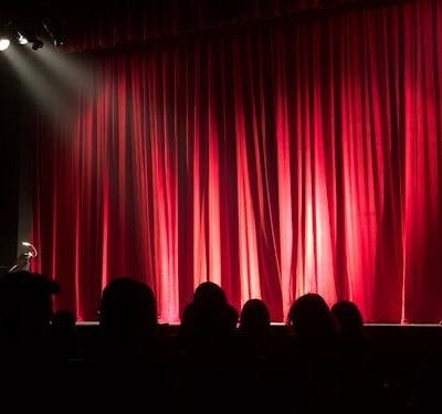Theatre stage with red curtains and spotlight creating dramatic atmosphere