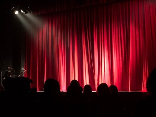 Theatre stage with red curtains and spotlight creating dramatic atmosphere