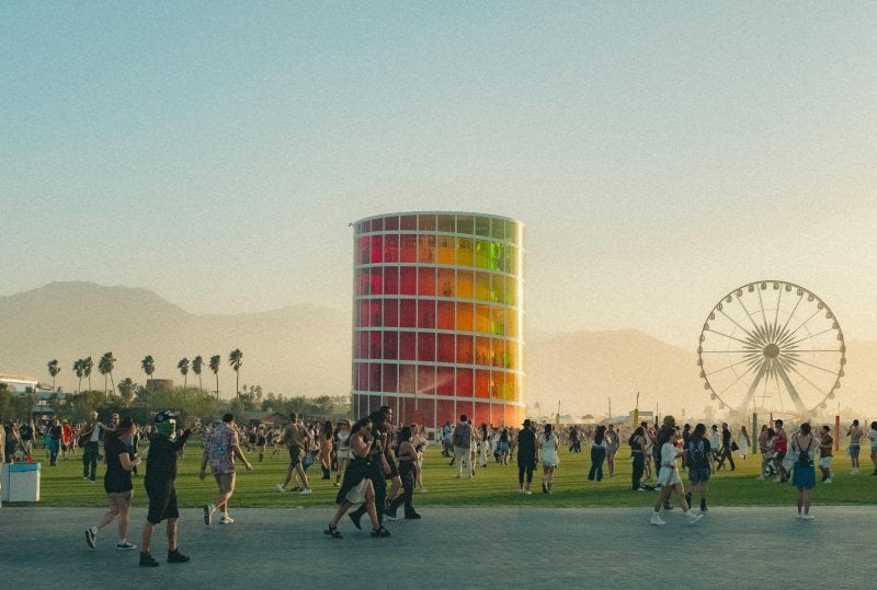 People enjoying a lively music festival with a colorful tower and Ferris wheel backdrop.