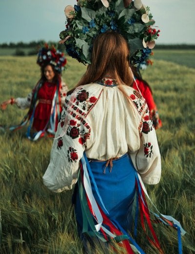 Two women in traditional floral on a summer field, celebrating culture.