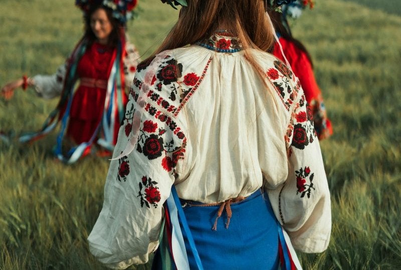 Two women in traditional floral on a summer field, celebrating culture.