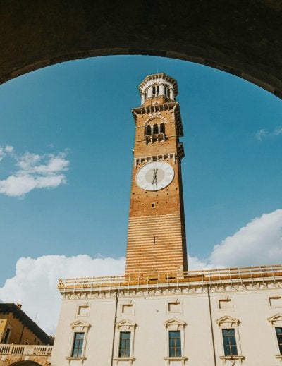 View of Lamberti Tower through archway in Verona, Italy with clear blue skies.