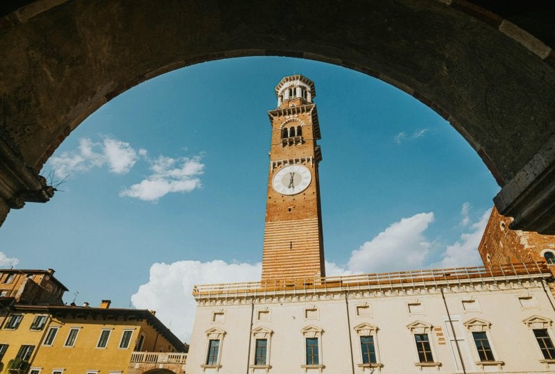 View of Lamberti Tower through archway in Verona, Italy with clear blue skies.