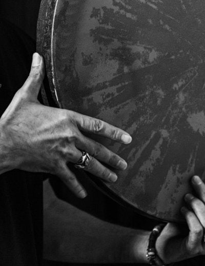 Black and white image capturing a musician holding and playing a large hand drum.