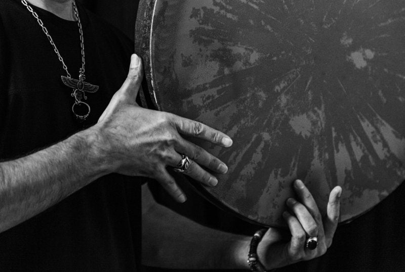 Black and white image capturing a musician holding and playing a large hand drum.