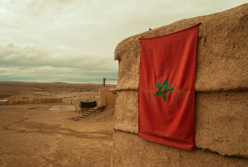 Moroccan flag hangs on a clay building in desert landscape