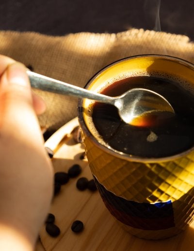 Female hand stirring with a spoon hot coffee in a yellow cup with Colombia flag in the morning
