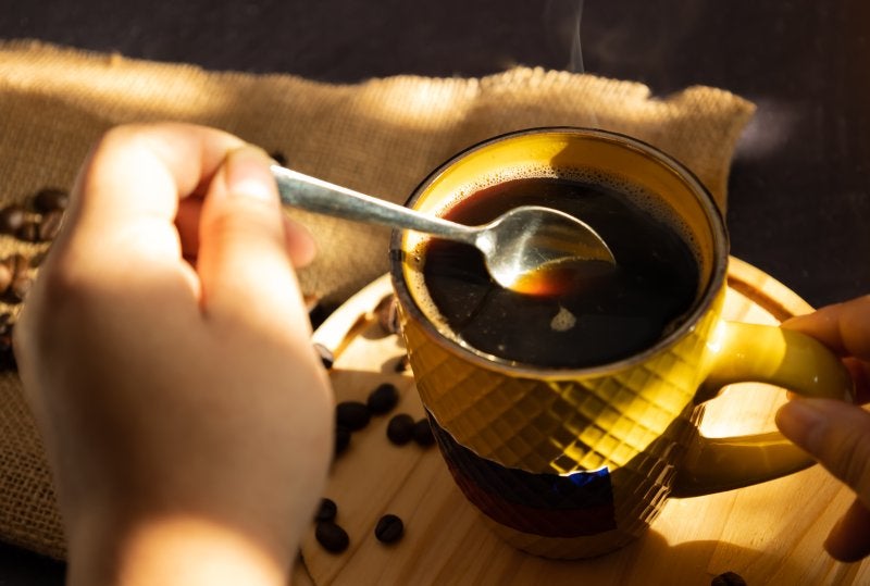 Female hand stirring with a spoon hot coffee in a yellow cup with Colombia flag in the morning