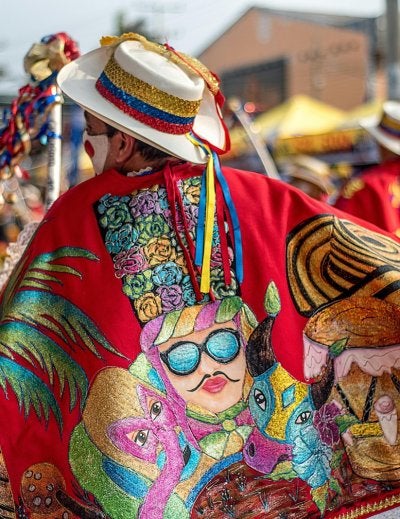 Vibrant festival scene featuring traditional Colombian dancers in colorful costumes with hats and capes.