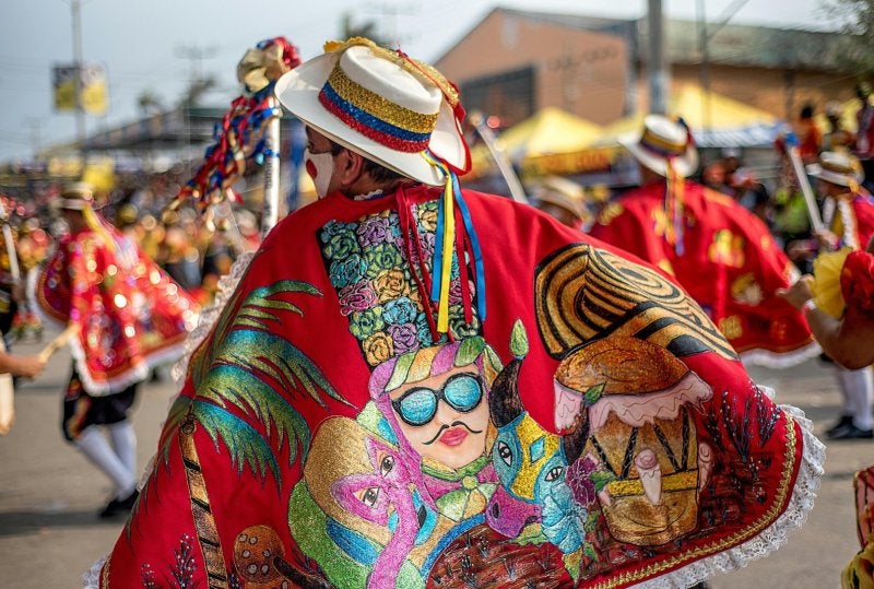 Vibrant festival scene featuring traditional Colombian dancers in colorful costumes with hats and capes.