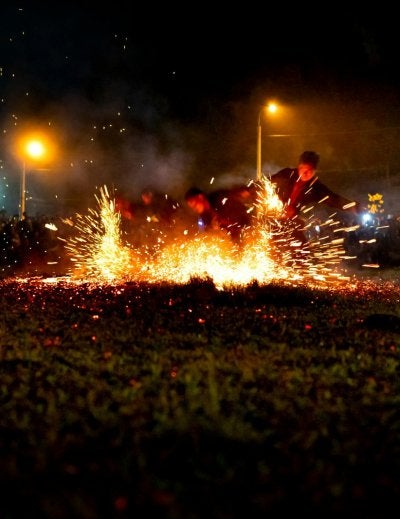 Group of fearless male dancers performing in sparkling bright lights of fire among crowd of people