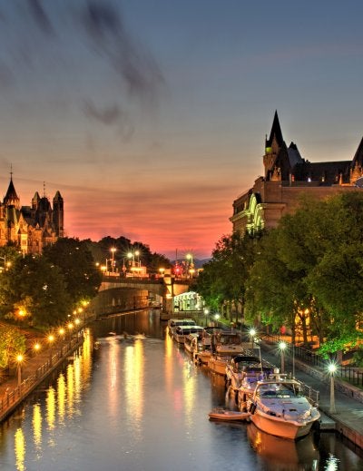 A beautiful warm orange-red glow fills the sky at dusk over Ottawa Canada during a July evening. A small wisp of low level clouds are visible. Parliament Hill, Chateau Laurier hotel and the Rideau Canal a UNSECO world heritage site are in the foreground.