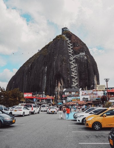 A captivating view of El Peñol Rock with cars parked around, showcasing the massive stone and its staircase path.