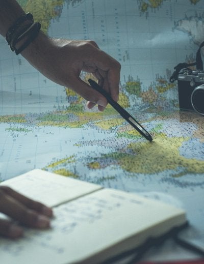 person pointing a pen on a map and writing on white paper